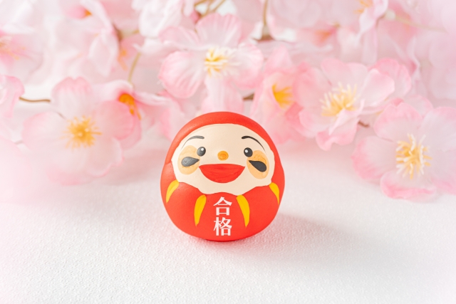 桜を背景に笑う合格だるま